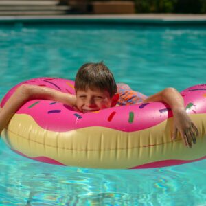 Young boy relaxing on a colorful donut floatie in a sunny swimming pool.