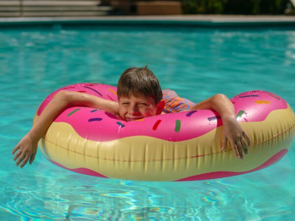 Young boy relaxing on a colorful donut floatie in a sunny swimming pool.